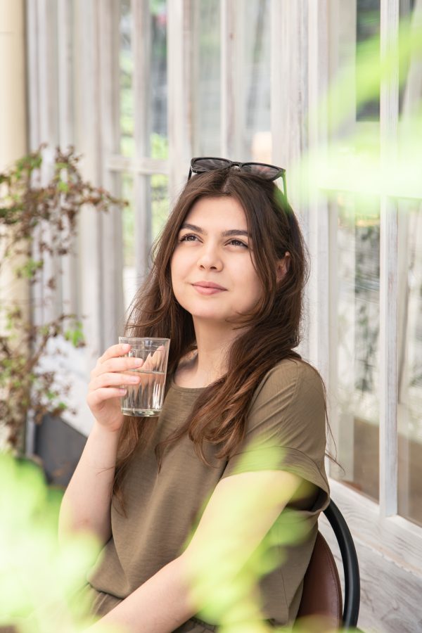 Attractive young woman with a glass of water on a summer day on a cafe terrace. Water Softening System
